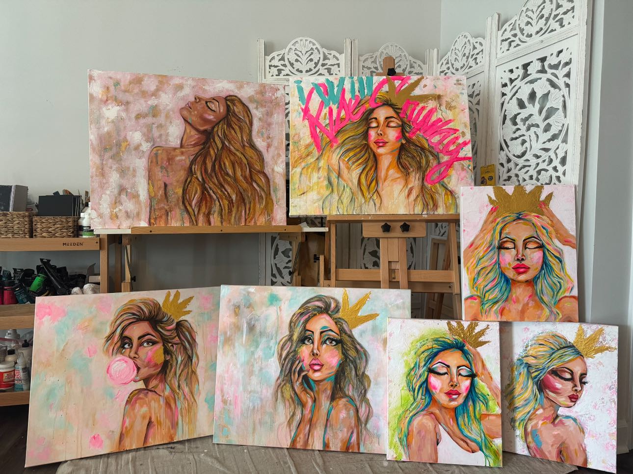 Collection of colorful paintings of women with crowns on a table.